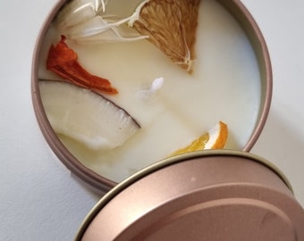 May include: A white candle with dried fruit and citrus slices in a rose gold tin.