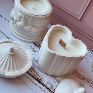 Puede incluir: Tres portavelas de cerámica blanca. Uno es un cilindro redondo con un diseño de carrusel, otro tiene forma de corazón y el tercero tiene forma de cúpula.
