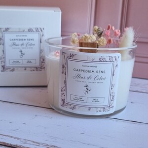 Pu&ograve; includere: Una candela bianca di cera di soia in un barattolo di vetro trasparente con un'etichetta bianca che recita "Carpediem Sens Fleur de Coton Cire de Soja - Parfum de Grasse Sans CMR - Sans parabens 140 gr - 45 Heures". La candela &egrave; decorata con fiori secchi e uno stoppino di legno.