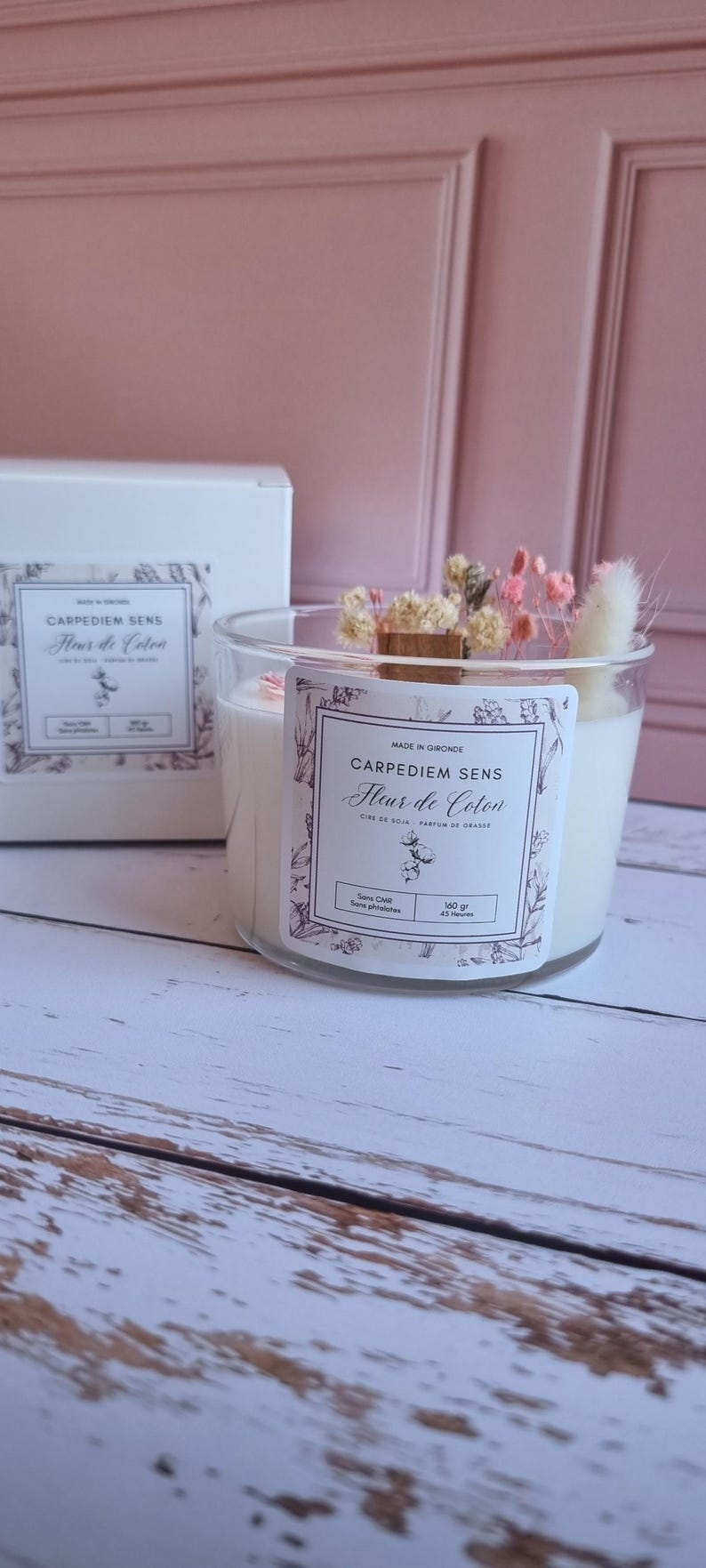Pu&ograve; includere: Una candela bianca di cera di soia in un barattolo di vetro trasparente con un'etichetta bianca che recita "Carpediem Sens Fleur de Coton Cire de Soja - Parfum de Grasse Sans CMR - Sans parabens 140 gr - 45 Heures". La candela &egrave; decorata con fiori secchi e uno stoppino di legno.