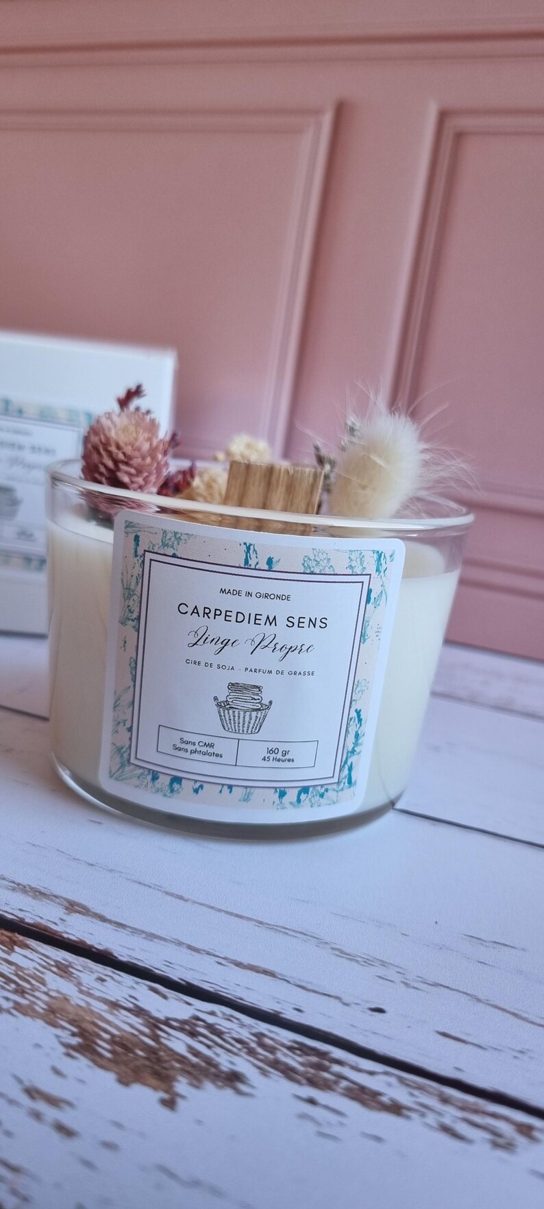 Pu&ograve; includere: Una candela bianca di cera di soia in un barattolo di vetro trasparente con un'etichetta decorativa. L'etichetta dice "Carpediem Sens Linge Propre" e "Cire de Soja - Parfum de Grasse". La candela &egrave; decorata con fiori secchi e un bastoncino di legno.
