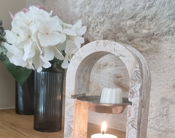 Peut inclure: Diffuseur en marbre blanc en forme d'arche avec une petite pastille de cire blanche et une bougie chauffe-plat. Le diffuseur est posé sur une surface en bois.