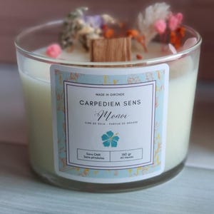 Pu&ograve; includere: Una candela in vetro trasparente con una base di cera di soia bianca e un'etichetta che recita "CARPEDIEM SENS Monoi CIPE DE SOJA - PARFUM DE GRASSE Sans CMR Sans phtalates 160 gr 45 Heures". La candela &egrave; decorata con fiori secchi e uno stoppino di legno.