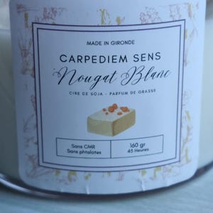 Pu&ograve; includere: Un barattolo di candela bianco con un'etichetta bianca che dice "CARPEDIEM SENS Nougat Blanc" in testo nero. L'etichetta dice anche "CIRE DE SOJA - PARFUM DE GRASSE" in testo nero pi&ugrave; piccolo. L'etichetta ha una piccola illustrazione di una barretta di torrone. L'etichetta dice anche "Sans CMR" e "Sans phtalates" in testo nero. L'etichetta dice anche "160 gr" e "45 Ore" in testo nero.