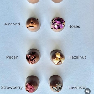 Puede incluir: Surtido de trufas de chocolate con varios ingredientes y rellenos. Sabores incluyen frambuesa, perlas crujientes, almendras, rosas, nueces, avellanas, fresas y lavanda. La imagen es un primer plano de las trufas.