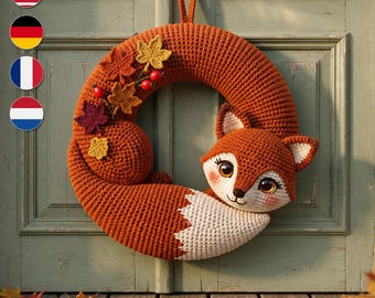 May include: A circular crochet wreath featuring a fox design with a large orange body, a white chest, and a long tail. The wreath is decorated with small crocheted autumn leaves in shades of yellow, orange, and dark red, along with tiny red berries.