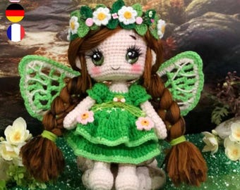Puede incluir: Muñeca de ganchillo hecha a mano con forma de hada. La muñeca tiene cabello castaño en trenzas, ojos verdes y un vestido verde con detalles florales. Tiene alas verdes y una corona floral. La muñeca está sentada sobre una piedra.