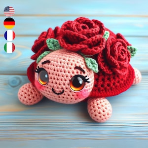 Op de afbeelding: Een gehaakt schildpad speelgoed met een roze lichaam en een rode schild. De schildpad heeft grote, zwarte ogen en een glimlachende mond. De schild is versierd met rode gehaakte rozen.