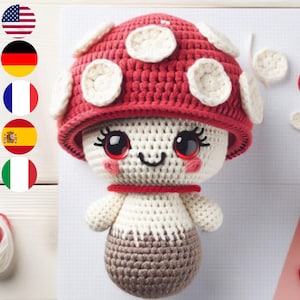 May include: A crocheted mushroom plush toy with a red and white cap and a white body. The mushroom has a smiling face with black eyes and eyelashes, and a red mouth. The toy is approximately 10 inches tall.