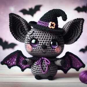 May include: A crocheted bat wearing a purple and black witch hat with a flower accent. The bat has large purple eyes and pink cheeks. The bat has purple wings.