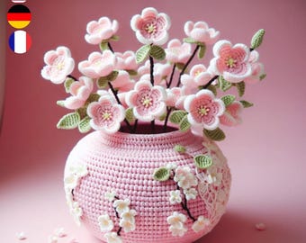 Könnte beinhalten: Eine rosa gehäkelte Vase mit einem Strauß rosa gehäkelter Blumen. Die Vase ist mit gehäkelten Blumen und Blättern verziert.