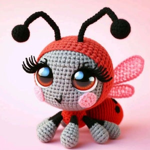 May include: A crocheted ladybug doll with a red body, head covering, and accents. The doll has large, expressive eyes, long eyelashes, and pink cheeks. Black antennae and legs complete the design. The wings are a light pink color.