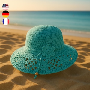 Könnte beinhalten: Ein türkisblauer Sonnenhut aus Häkelarbeit mit breiter Krempe und Blumenmuster. Der Hut liegt auf einem Sandstrand mit dem Meer im Hintergrund. Der Hut hat eine dekorative Blume und eine Perlenschnur.