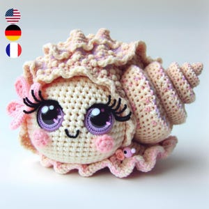 May include: A crocheted seashell with a pink flower and large eyes. The seashell is cream coloured with pink accents.