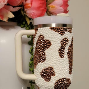 May include: A white ceramic mug with a black handle and the text "But first, coffee" in a handwritten style. The mug is on a white surface. The mug is approximately 4 inches tall.