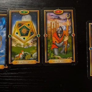 May include: Four tarot cards are displayed, each with a black border and gold accents. The cards feature illustrations of swords, pentacles, and wands, with titles like "Ace of Swords" and "Nine of Wands". The artwork includes a sword, a fox, and a knight.