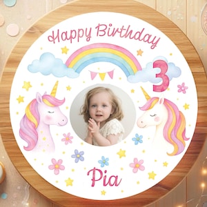 May include: A round, wooden cake topper with a watercolor design. The design includes a photo of a child, two unicorns, a rainbow, clouds, stars, flowers, and the text "Happy Birthday" and "Pia 3".