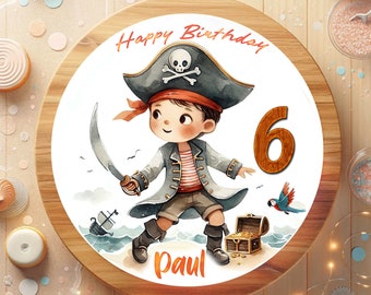 May include: A round wooden cake board with a white background featuring a cartoon pirate holding a sword. The pirate is wearing a blue and red hat with a skull and crossbones. The text "Happy Birthday" is written in red above the pirate and the number "6" is written in brown to the right of the pirate. The text "Paul" is written in orange below the pirate.