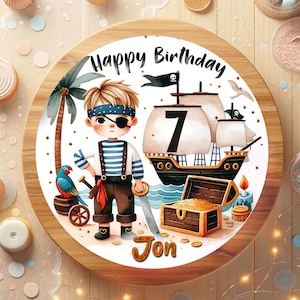 May include: A round cake decorated with a pirate theme. The design includes a cartoon pirate, a ship, a treasure chest, and the text "Happy Birthday" and "Jon". The number "7" is also visible on the cake.