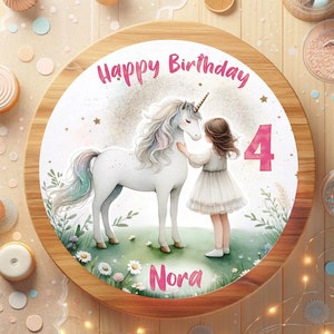 Könnte beinhalten: Ein runder Holz-Kuchentopper mit weißem Hintergrund, auf dem ein Einhorn und ein Mädchen zu sehen sind. Das Einhorn ist weiß mit einer Regenbogenmähne und einem Regenbogen-Schwanz. Das Mädchen trägt ein weißes Kleid und hat lange braune Haare. Der Text "Happy Birthday" ist in Pink oben auf dem Topper geschrieben. Die Zahl "4" ist in Pink auf der rechten Seite des Toppers geschrieben. Der Name "Nora" ist in Pink unten auf dem Topper geschrieben.