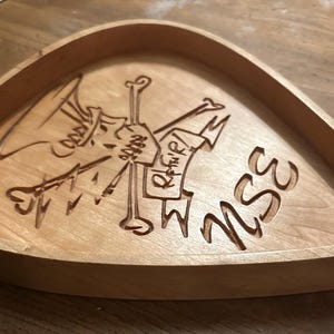 May include: A wooden tray shaped like a guitar pick with a carved image of a skull and crossbones and the word "MUSE" on the bottom.