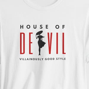 Top line of shirt reads HOUSE OF, followed by the word DE VIL, with the silhouette of a woman in between the E and the V. Below are the words Villainously Good Style. Shown is the Solid White Blend shirt color option.