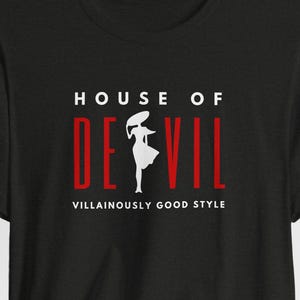 Top line of shirt reads HOUSE OF, followed by the word DE VIL, with the silhouette of a woman in between the E and the V. Below are the words Villainously Good Style. Shown is the Black Heather shirt color option.