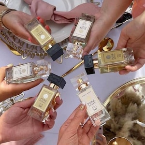 May include: Five glass bottles of perfume with gold labels and black caps. The labels read "Pure Royal" and have a number on each bottle. The bottles are being held by multiple hands.