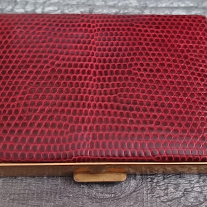 May include: A red leather compact with a gold trim and a snakeskin pattern.
