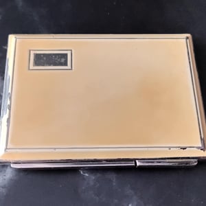 May include: A silver compact with a cream-coloured interior and a small rectangular inscription that reads "Visa".