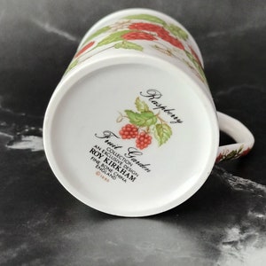 K&ouml;nnte beinhalten: Wei&szlig;e Keramiktasse mit einem roten und gr&uuml;nen Himbeerdesign. Die Tasse tr&auml;gt die Aufschrift "Fruit Garden" und "Roy Kirkham" sowie den Text "An Exclusive Design Fine Bone China England &copy;1990".