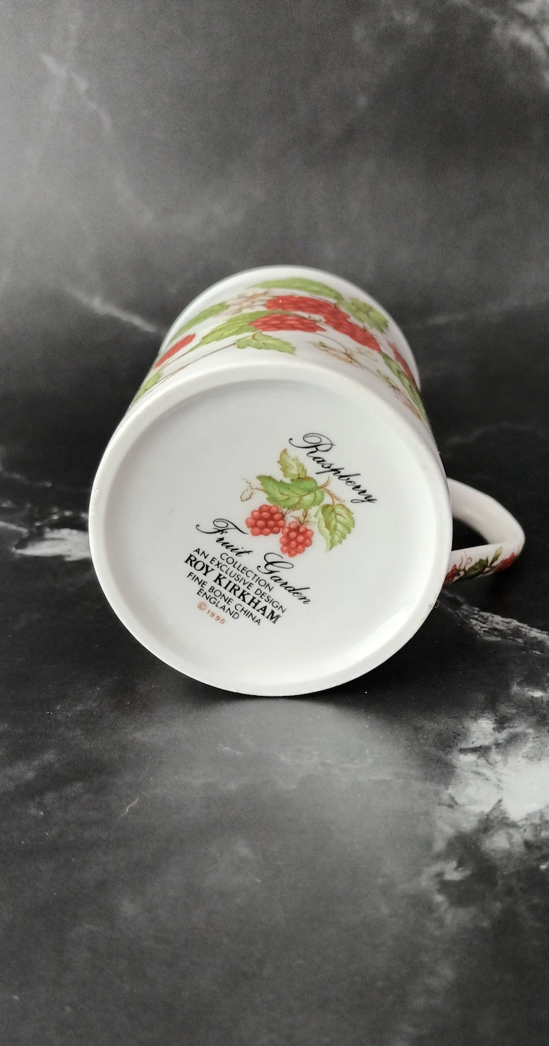 K&ouml;nnte beinhalten: Wei&szlig;e Keramiktasse mit einem roten und gr&uuml;nen Himbeerdesign. Die Tasse tr&auml;gt die Aufschrift "Fruit Garden" und "Roy Kirkham" sowie den Text "An Exclusive Design Fine Bone China England &copy;1990".