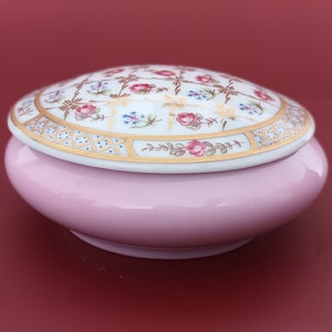 May include: A pink porcelain trinket box with a white lid featuring a floral design in gold, pink, and blue.
