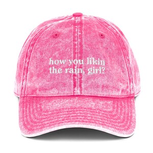 May include: Pink vintage washed cotton baseball cap with white embroidered text that reads "how you likin the rain, girl?"