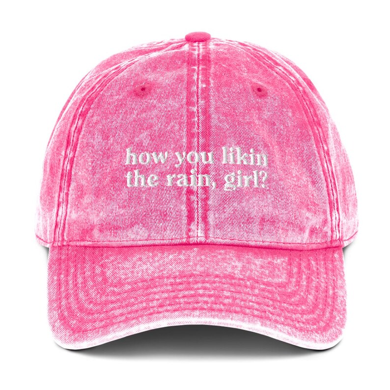 May include: Pink vintage washed cotton baseball cap with white embroidered text that reads "how you likin the rain, girl?"