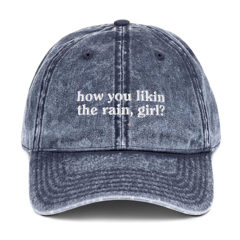 May include: A blue denim baseball cap with the text "how you likin the rain, girl?" embroidered in white.