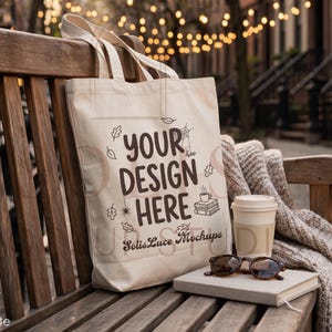 May include: A cream-colored canvas tote bag featuring dark brown text that reads YOUR DESIGN HERE and SolisLuce Mockups, accompanied by small illustrations of leaves, a spider web, a spider, a coffee cup, and a stack of books.