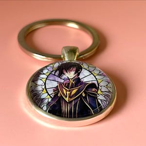 Könnte beinhalten: Ein runder Metallschlüsselanhänger mit einem Glaskabochon, der eine dunkelhaarige Figur in einer violett-goldenen Uniform zeigt. Die Figur ist vor einem kreisförmigen Hintergrund im Buntglasstil mit weißen und violetten Segmenten platziert.