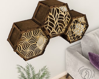 Puede incluir: Tres estantes hexagonales de madera con diferentes diseños de corte láser. Los estantes están montados en una pared blanca. Los estantes están hechos de madera marrón oscura con un diseño de corte láser marrón claro.
