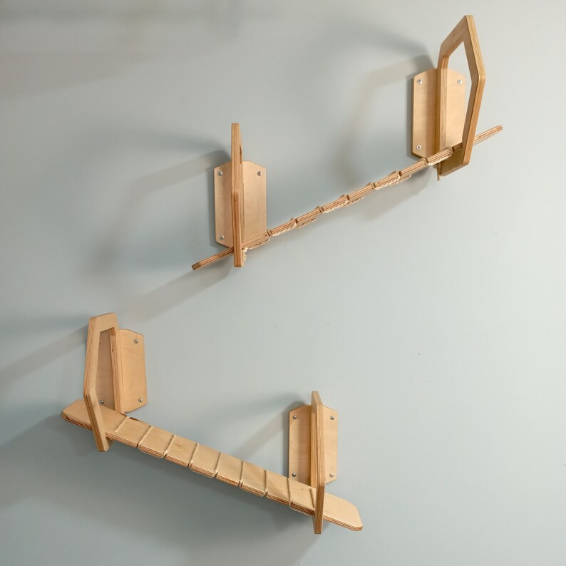 May include: Three wooden cat climbing shelves mounted on a light blue wall. The shelves are made of natural wood and have a simple design. The top shelf has a rope bridge connecting the two sides. The middle shelf is a ramp that slopes down. The bottom shelf is a flat platform.