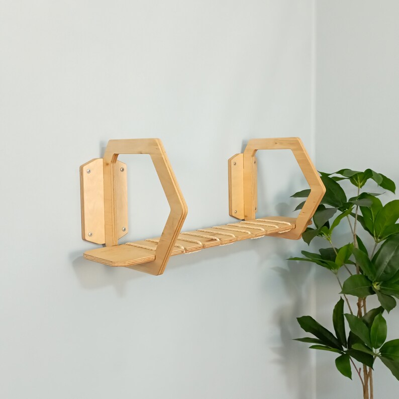 May include: A wooden hexagonal shelf with a natural finish. The shelf has a small ledge and a series of rope rungs. The shelf is mounted on a wall.