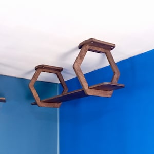 Puede incluir: Dos estantes hexagonales de madera montados en una pared azul. Los estantes están conectados por una sola tabla de madera.