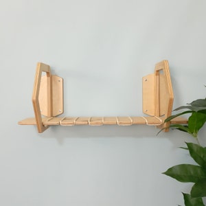 May include: A wooden shelf with a unique geometric design, featuring a natural wood finish and a white rope detail. The shelf is mounted to a light blue wall.
