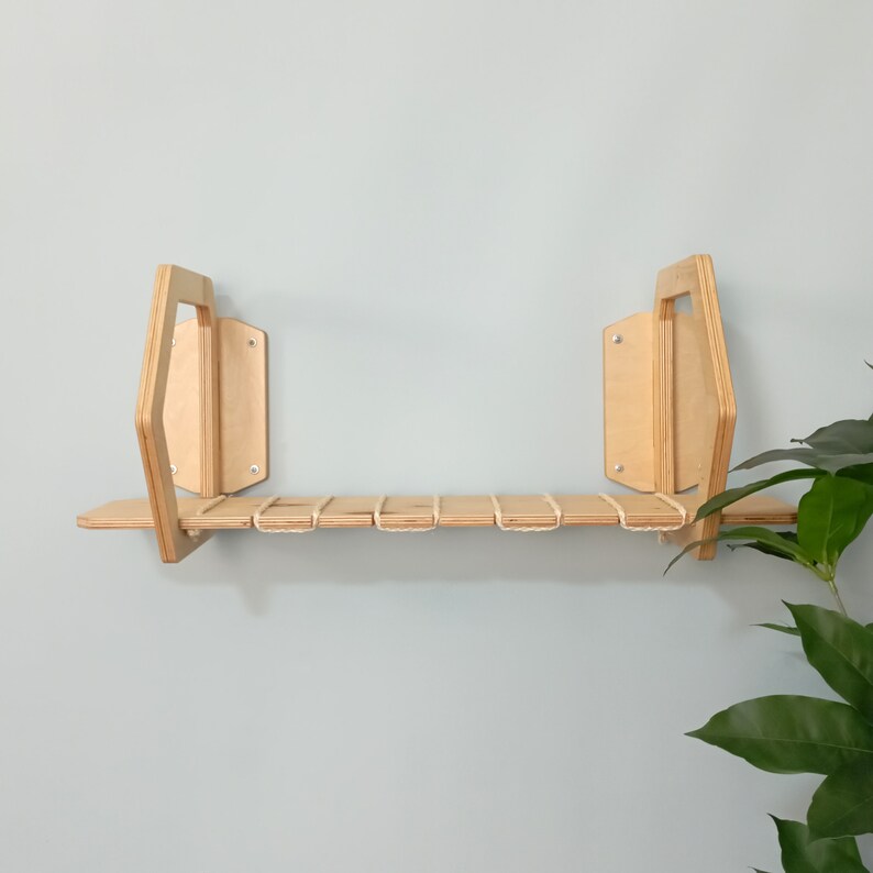 May include: A wooden shelf with a unique geometric design, featuring a natural wood finish and a white rope detail. The shelf is mounted to a light blue wall.