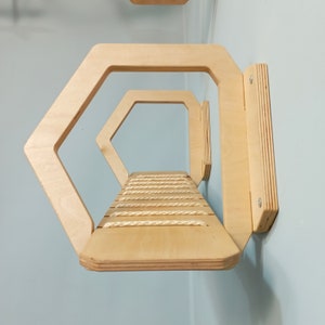 May include: A wooden cat shelf with a rope-covered platform. The shelf is shaped like a hexagon and has two levels. The shelf is mounted to a wall.