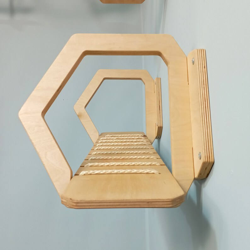 May include: A wooden cat shelf with a rope-covered platform. The shelf is shaped like a hexagon and has two levels. The shelf is mounted to a wall.