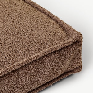 May include: A brown, fluffy, square floor cushion with a stitched seam around the edges.
