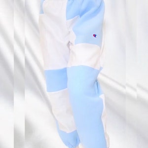 May include: Color-block sweatpants in white and light blue, featuring a Champion logo on the leg. The waistband is black with white text that reads "NIKE PRO N". The pants have elastic cuffs at the ankles.