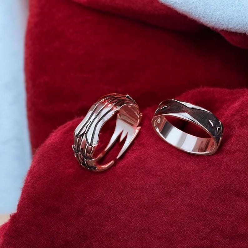 May include: Two silver rings on a red velvet background. One ring has a claw design and the other is a simple band.