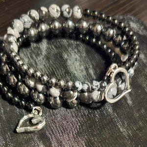 May include: A multi-strand bracelet with black and white beads and a silver heart charm.